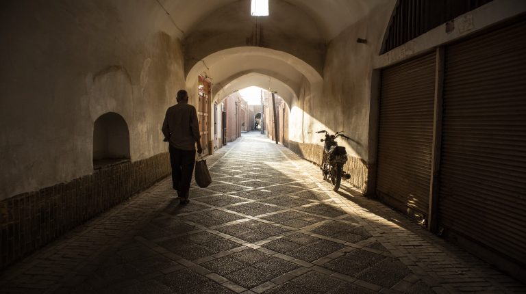 mężczyzna idzie wąską uliczką w yazd, w iranie.