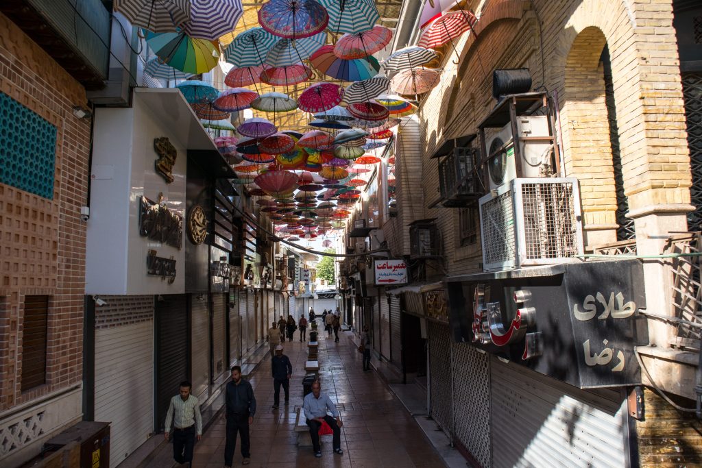 men and women walk along an alley in shiraz with umbrellas hanging over them 