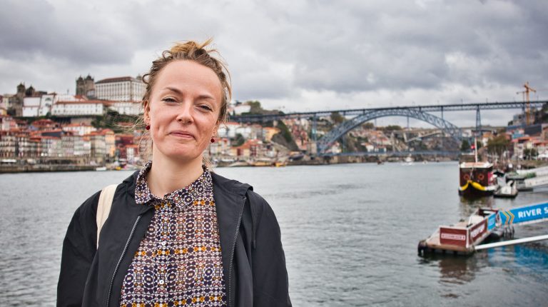 a girl stands at the river in porto smiling lightly on a cloudy day