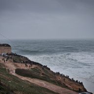 crowds of people standing on a hill and watching the waves in nazare