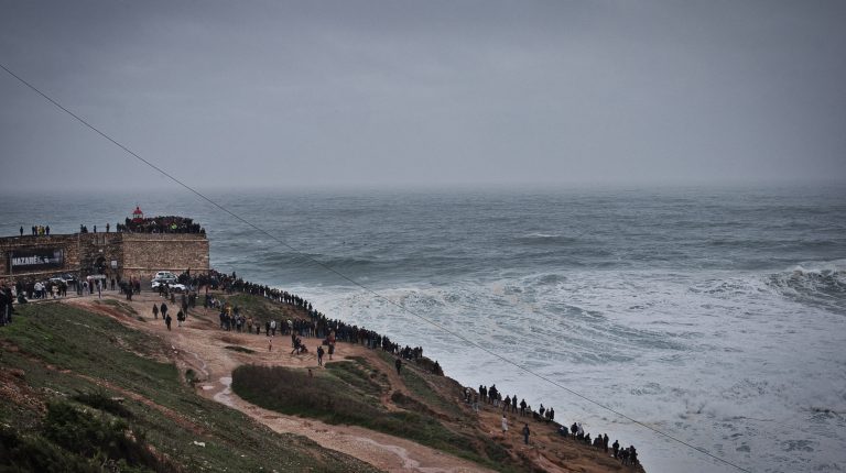 crowds of people standing on a hill and watching the waves in nazare