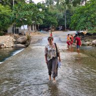 a woman dressed in a flowery shirt walks through the stream in thailand