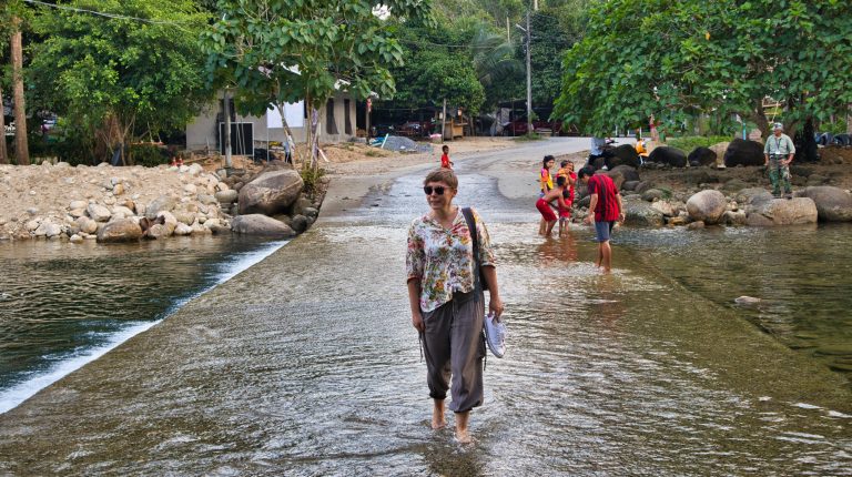 a woman dressed in a flowery shirt walks through the stream in thailand