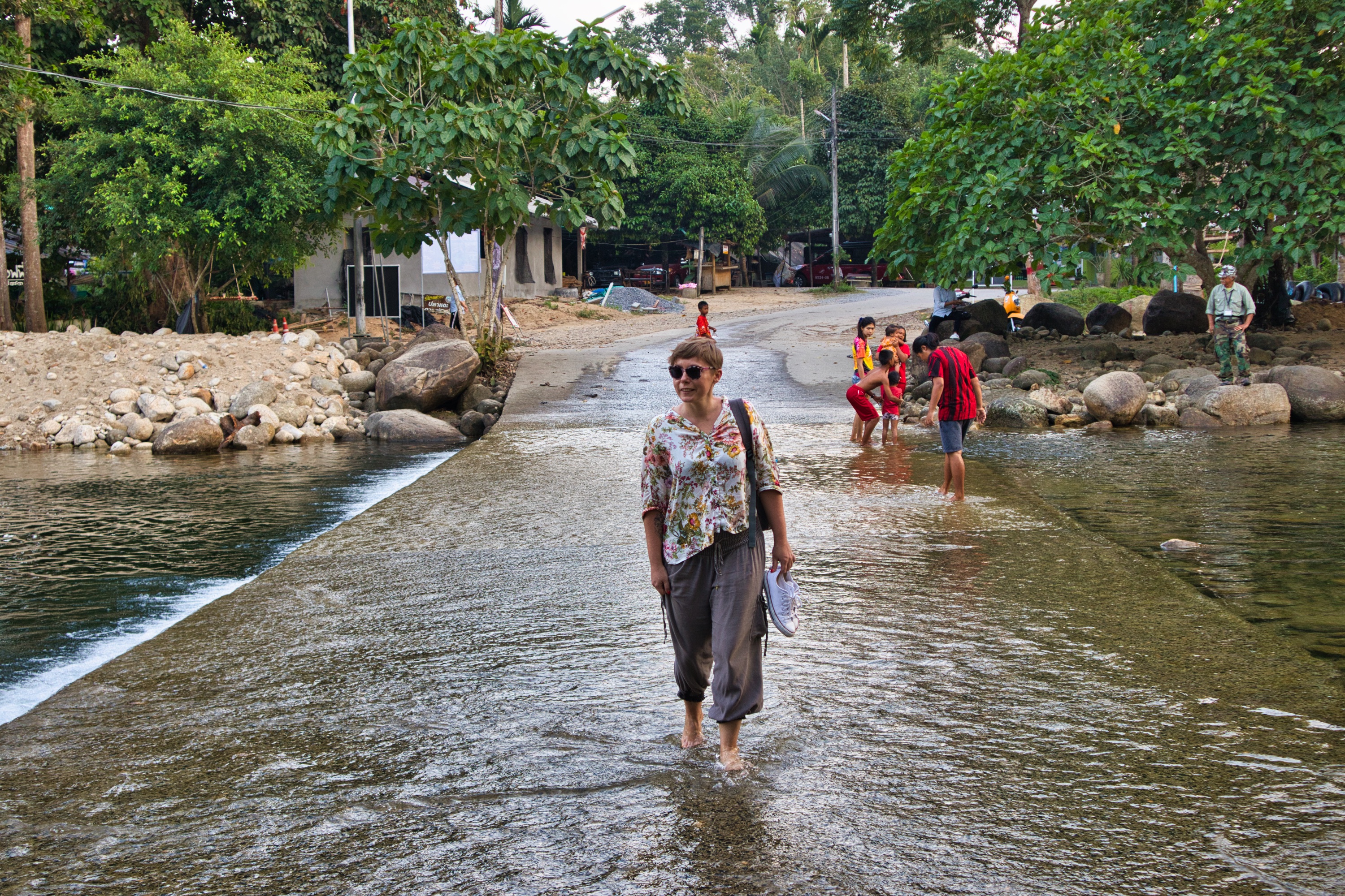 a woman dressed in a flowery shirt walks through the stream in thailand