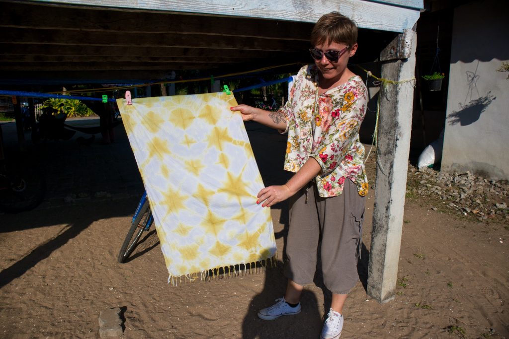 a woman dressed in a flowery blouse holding a scarf with yellow patterns. she smiles. thailand, krabi, koh klang, thai dye. 