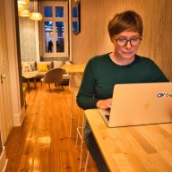 insurance digital nomads. A woman in a green jumper sits in front of a computer in a room.
