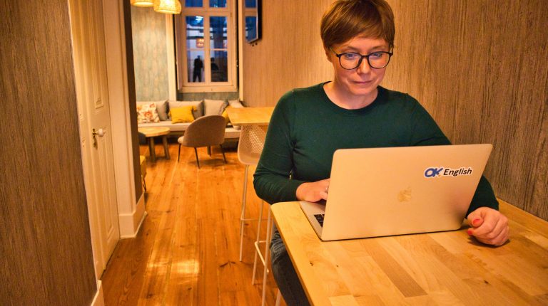 insurance digital nomads. A woman in a green jumper sits in front of a computer in a room.