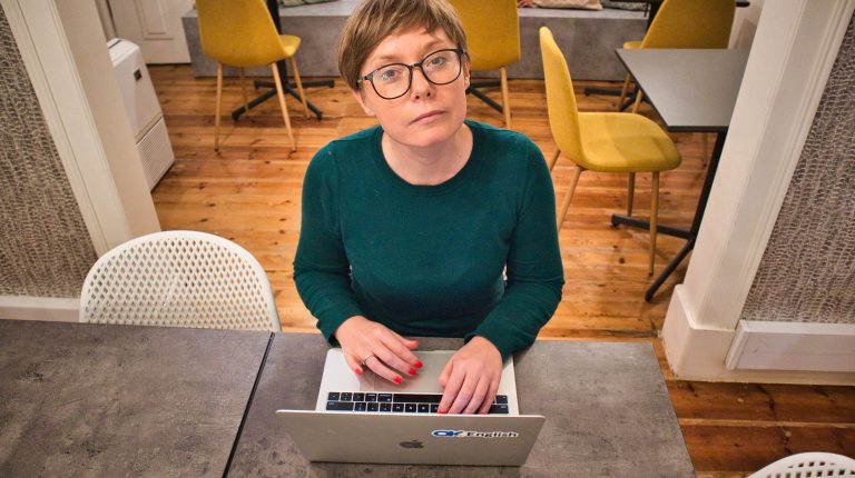 a girl sitting in front of her computer looking up at a camera. digital nomad travel insurance.