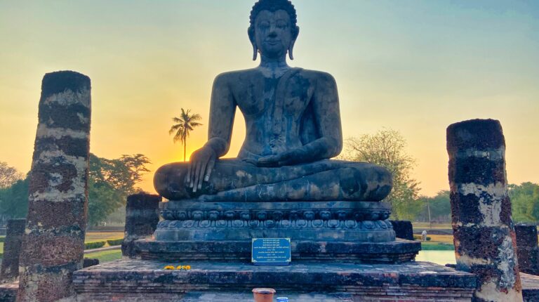 posąg buddy siedzącego na kamieniu przy zachodzie słońca