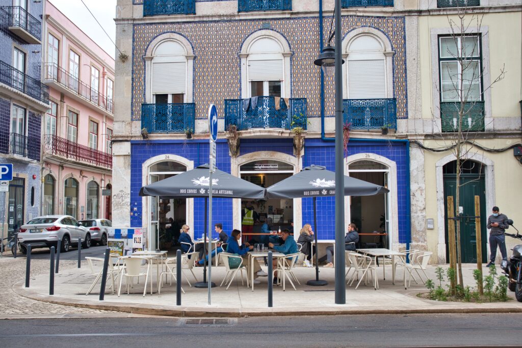 Kamienica w Lizbonie z niebieskim azulejo. Przed nią stoją parasole i przy stolikach siedzą ludzie. Neighbourhood, Lizbona.