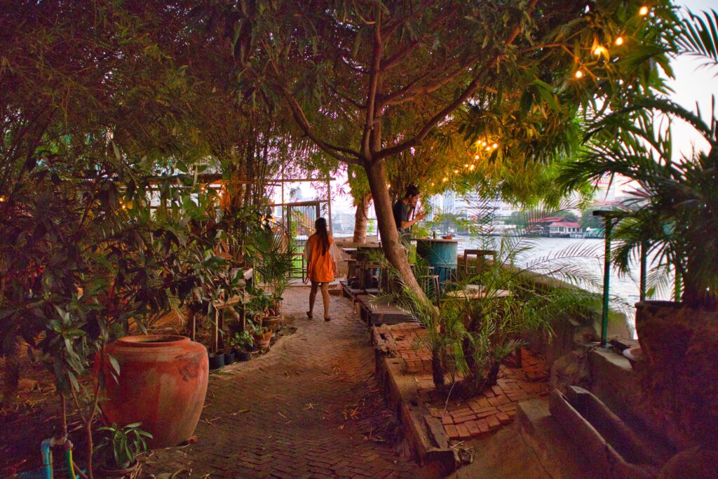 a woman walking in a small garden, in river vibe restaurant, talad noi, bangkok.