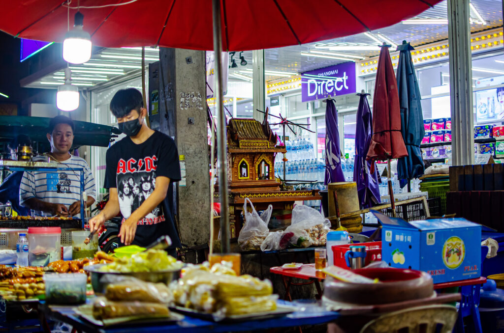 Dwóch młodych Tajów stoi przy stoisku z jedzeniem na Chiang Mai Gate Market. 